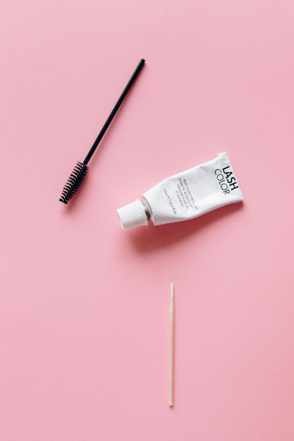 Top view of eyelash cosmetic tube and brush on a pink background, perfect for beauty concept.